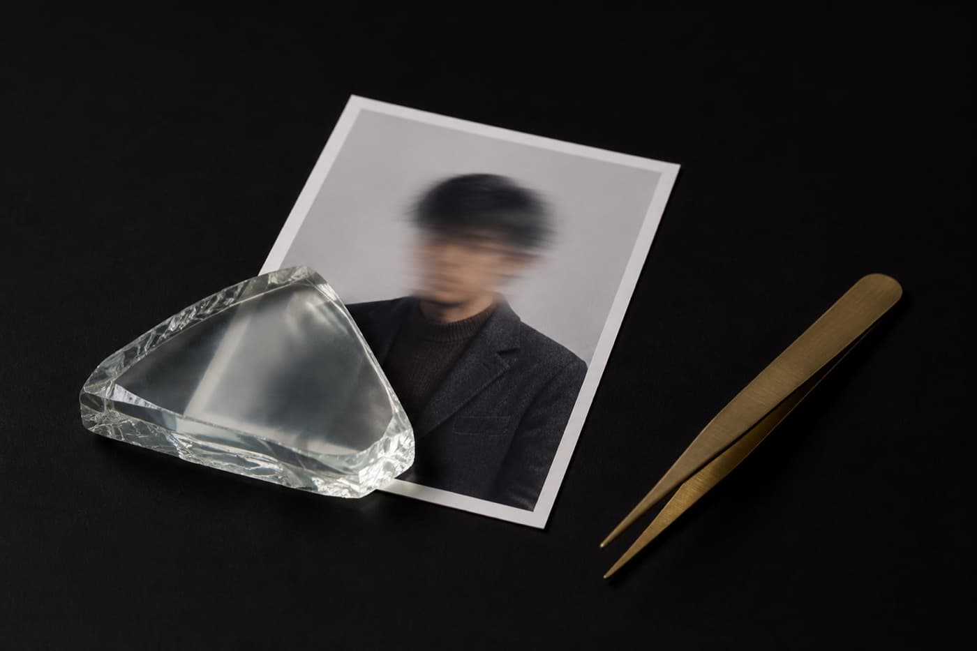 검은 테이블 위 작은 인화 사진의 왼쪽 아래 모서리에 반투명 유리 조각이 얹혀 그 부분만 뿌옇게 비쳐 보이고 옆에 황동 핀셋이 놓여 있다