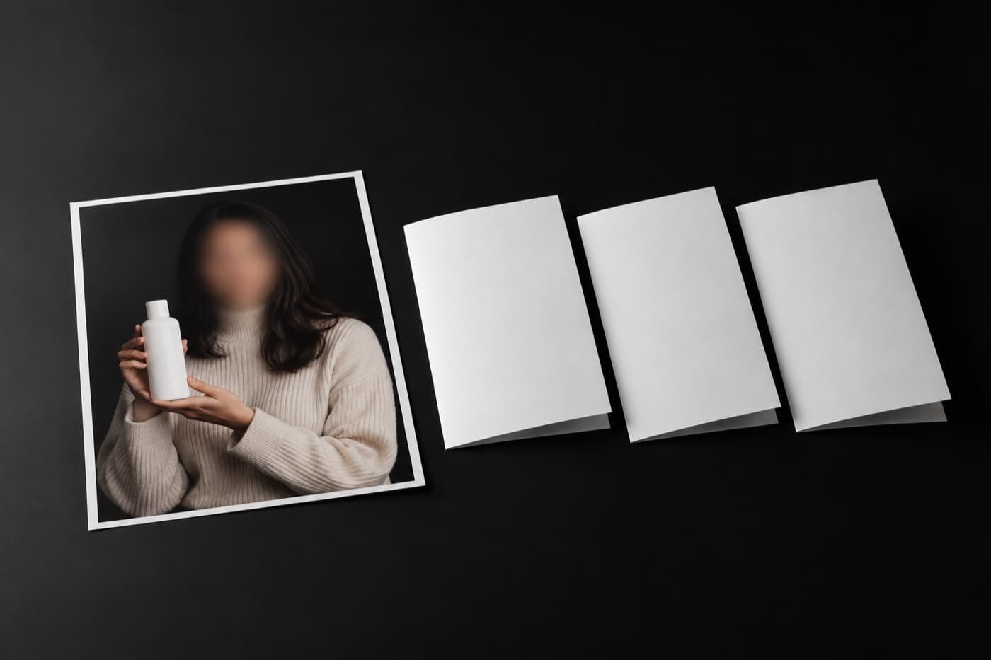 검은 테이블 위 왼쪽에 얼굴이 흐릿한 인물이 무지 제품 병을 든 인화 사진 한 장, 오른쪽에 접힌 빈 흰 종이 세 장이 조금씩 어긋나게 나란히 놓여 있다